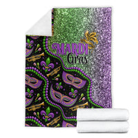 Mardi Gras themed blanket folded, glitter green and purple front with mask and bead graphics