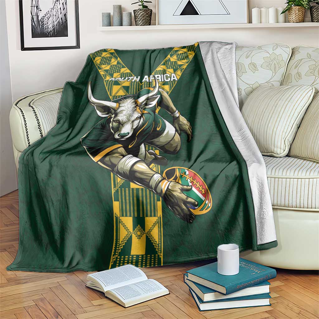 Green rugby blanket on a couch with South Africa text, ox head, rugby ball, and yellow design
