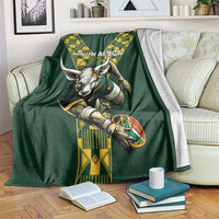 Green rugby blanket on a couch with South Africa text, ox head, rugby ball, and yellow design