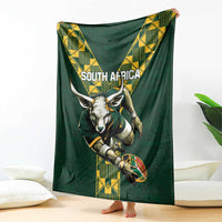 Green rugby blanket draped with South Africa text, ox head, and yellow geometric stripe design