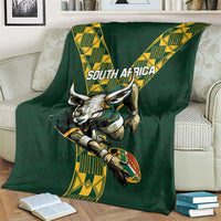 Green rugby blanket folded on a sofa showing South Africa text, ox head, and yellow patterns