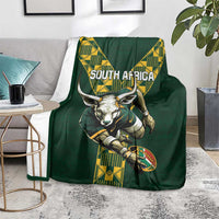 Green rugby blanket on a floor with South Africa text, ox head, and yellow geometric panel