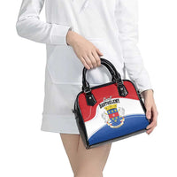 Shoulder bag in red, white, and blue with black handles and crest emblem