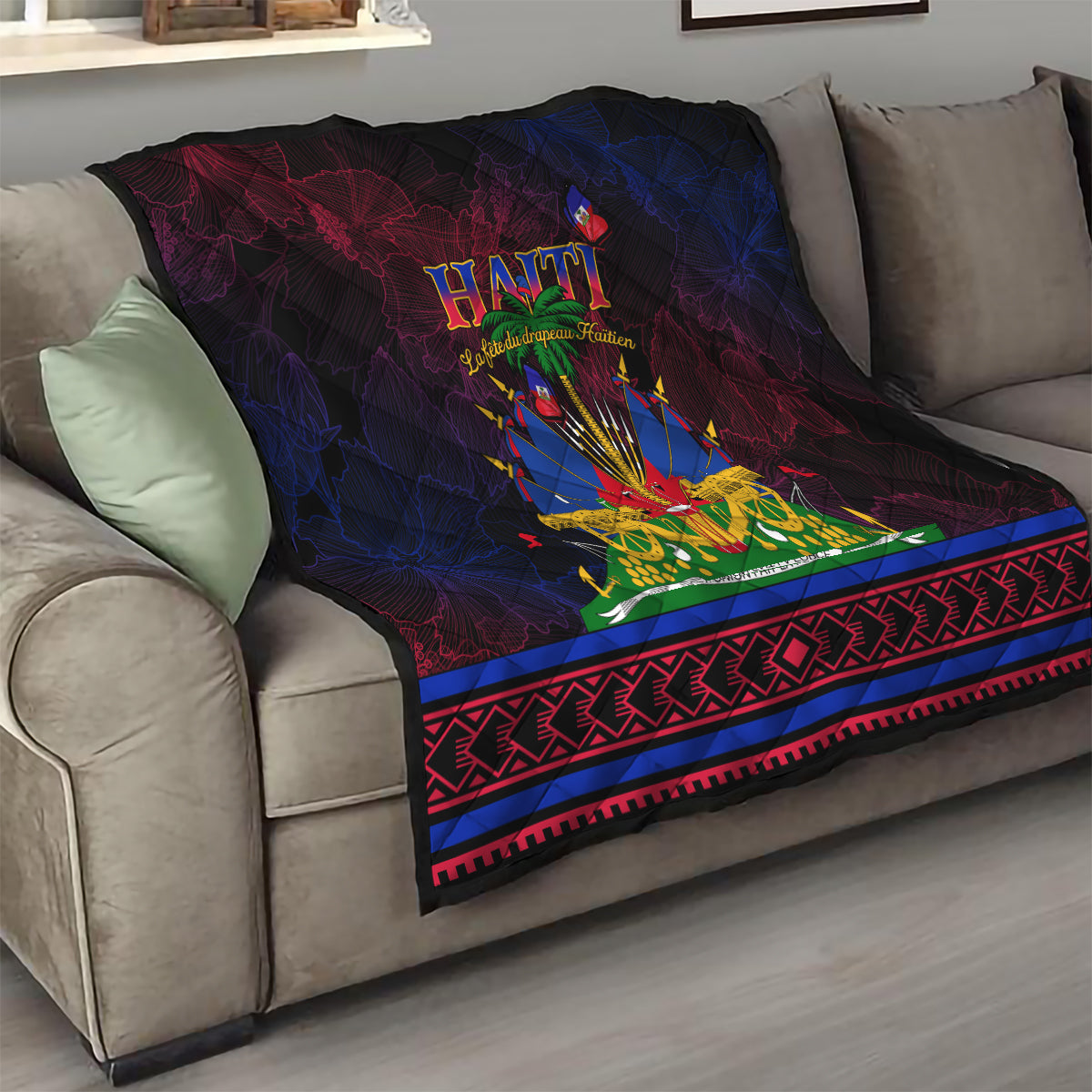 Haitian Flag Day quilt draped on sofa with central Haiti emblem and red/blue geometric border, dark quilt.