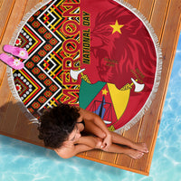 Round fringed beach blanket laid flat, featuring Cameroon coat-of-arms and red Ankara pattern