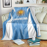 Blue and white Argentina football blanket with sun emblem and stripes, draped on sofa.