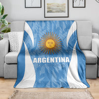 Argentina football blanket, blue with white V stripes and sun crest, laid over gray sofa.