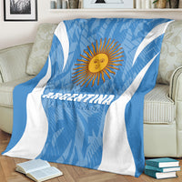 Blue and white Argentina football blanket with sun emblem, draped across beige sofa.