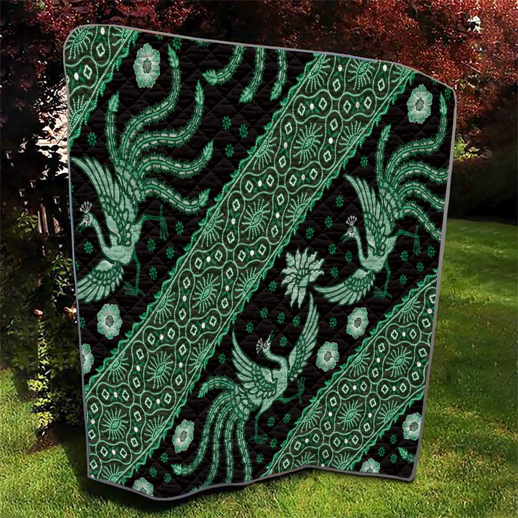 Green and black batik pattern quilt spread on grass, showing dragon and floral motifs
