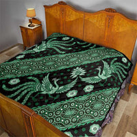 Green and black batik pattern quilt on wooden bed with dragon and floral motifs