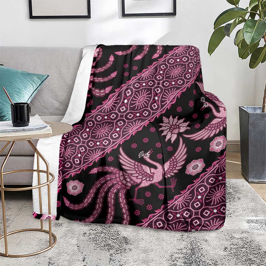 Batik pattern blanket folded on floor, pink bird and floral motifs on dark fabric with fringe