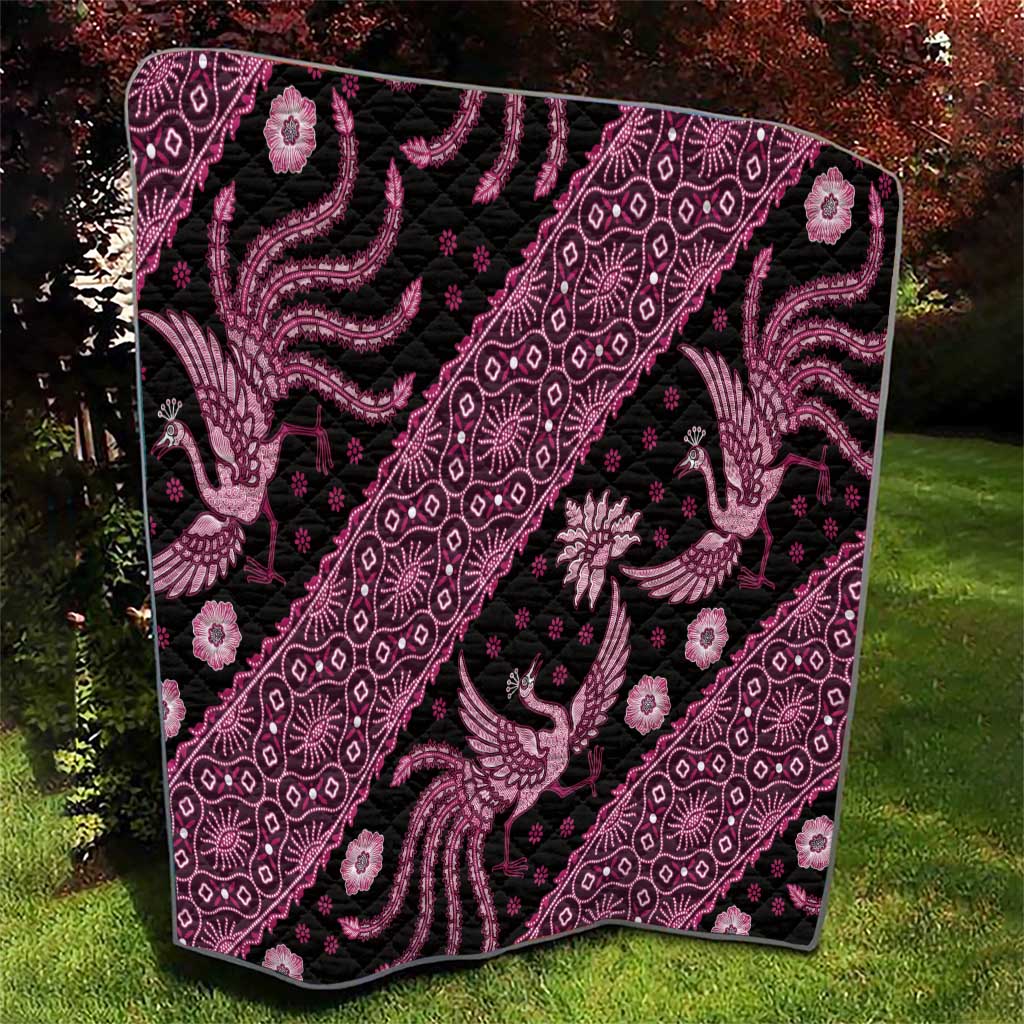 Pink and black batik-pattern quilt folded on grass, ornate peacock and diamond medallions.