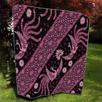 Pink and black batik-pattern quilt folded on grass, ornate peacock and diamond medallions.