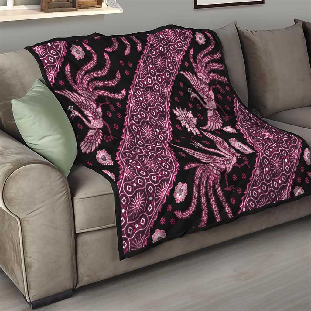 Pink and black batik-pattern quilt draped over a sofa, showing peacock and floral motifs.