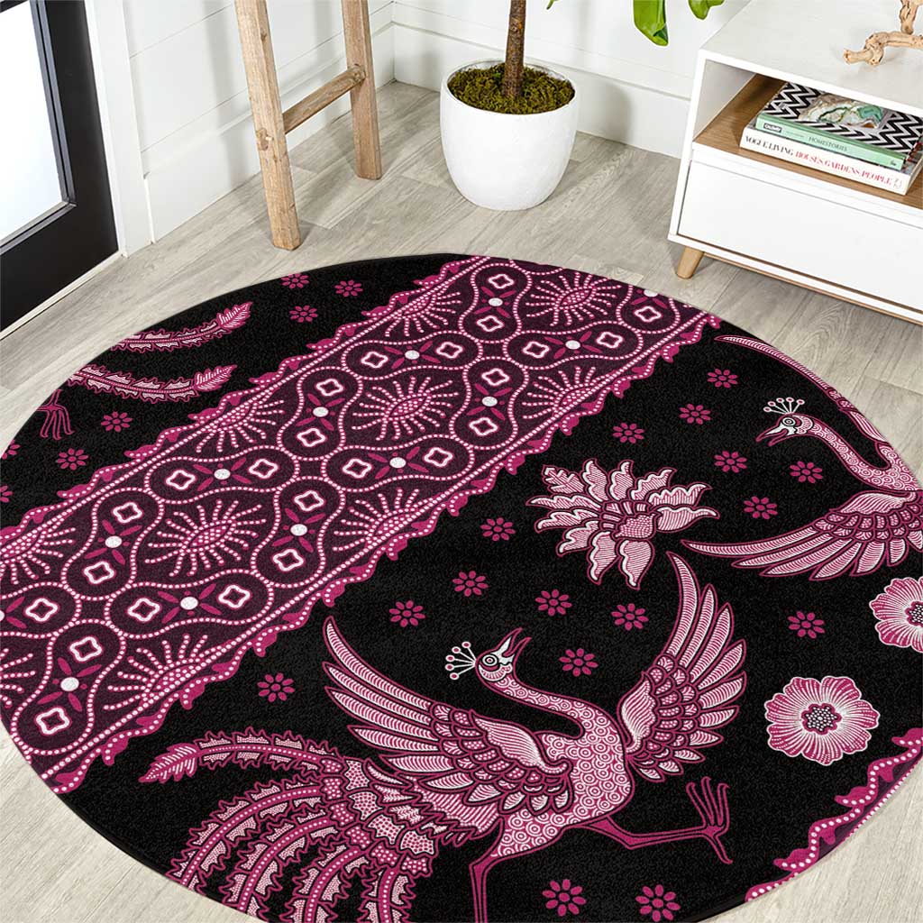 Pink round batik-pattern area rug with bird and floral motifs on dark background.
