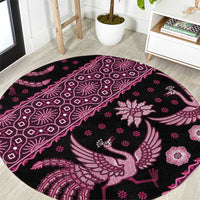 Pink round batik-pattern area rug with bird and floral motifs on dark background.