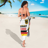 White sarong worn as a wrap, featuring Unity Day 1990 emblem and flag stripes