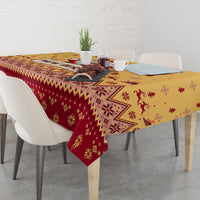 Christmas tablecloth covering table with gold-and-red border, reindeer and tree motifs