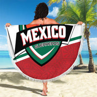 Round fringed beach blanket with Mexico Guerreros banner logo, held on sandy beach
