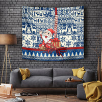 Blue holiday tapestry with Santa holding a gift, framed by winter reindeer and snowflake pattern