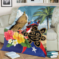 Blue blanket over sofa arm featuring El Morro tower, coqui frog, palm leaves, flowers, star