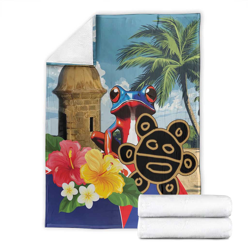 Blue blanket with El Morro tower, coqui frog and palm leaves, shown with folded white towels