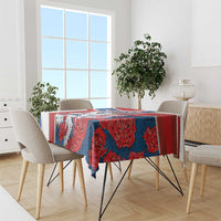Red and blue lion-and-rose patterned tablecloth on dining table with chairs.