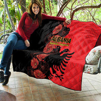 Folded quilt blanket draped on patio seating, black and red with Albania crest and flowers.
