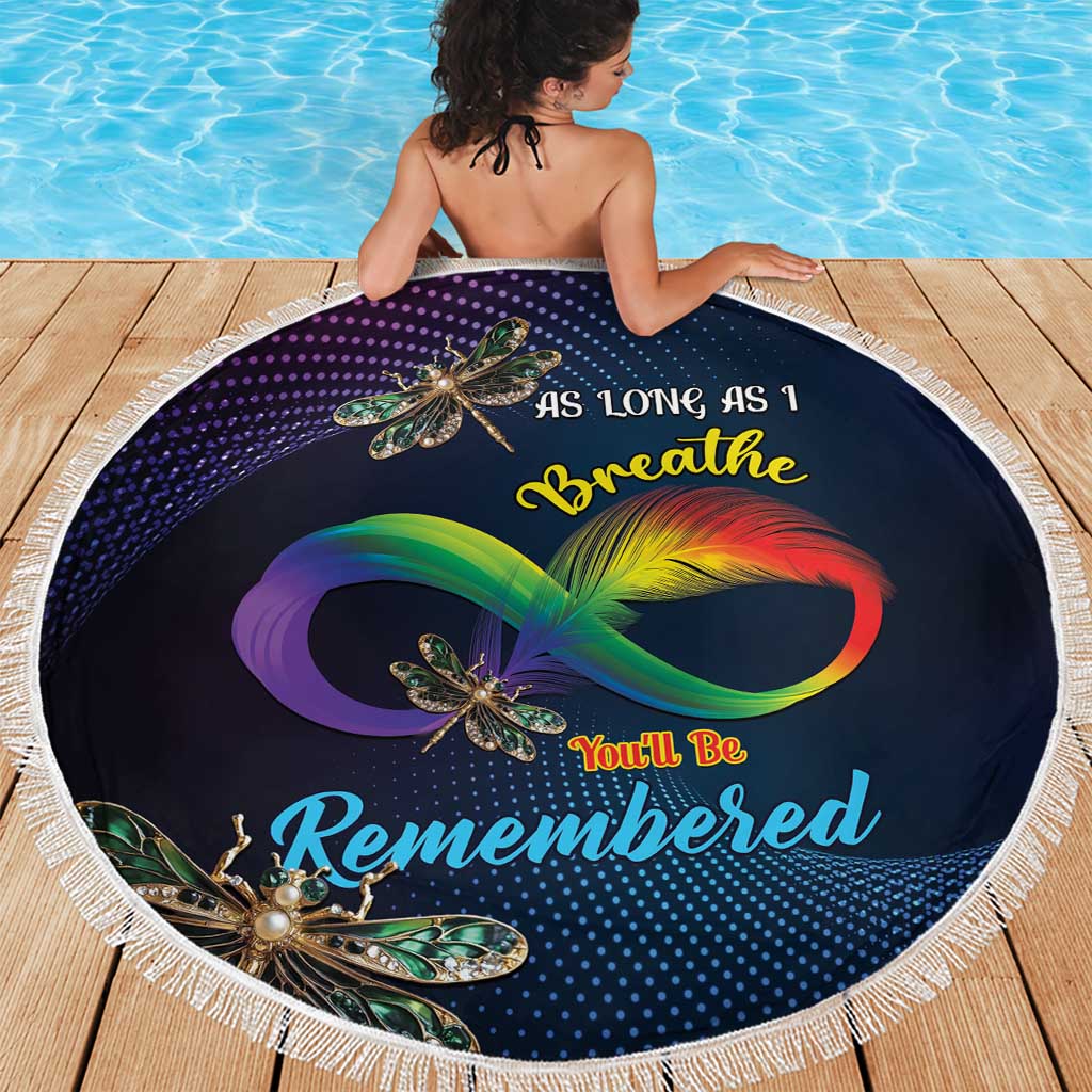 Round navy beach blanket with dragonfly artwork and white fringe, laid on wooden deck