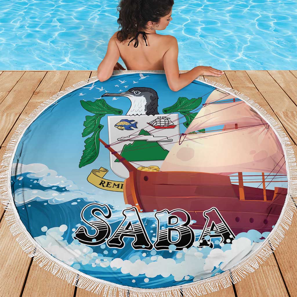 Blue round Saba beach blanket showing sailboat, waves, and leaf graphic; fringed edge.