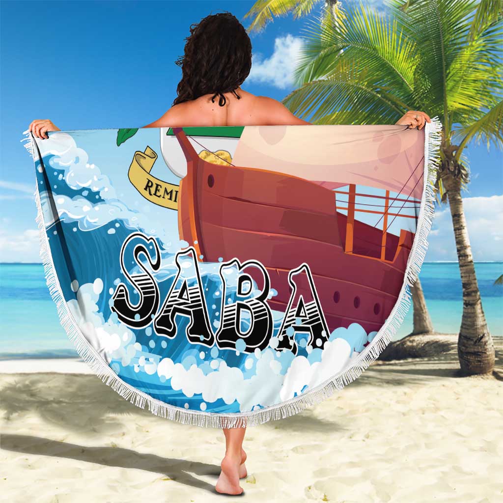 Round Saba beach blanket with sailboat and SABA lettering, white fringe trim.