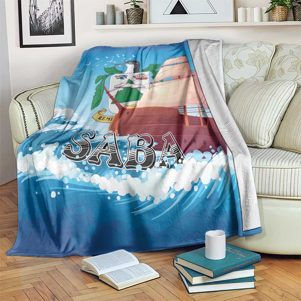 Blue blanket with sailboat graphic and “SABA” lettering, shown draped over a couch