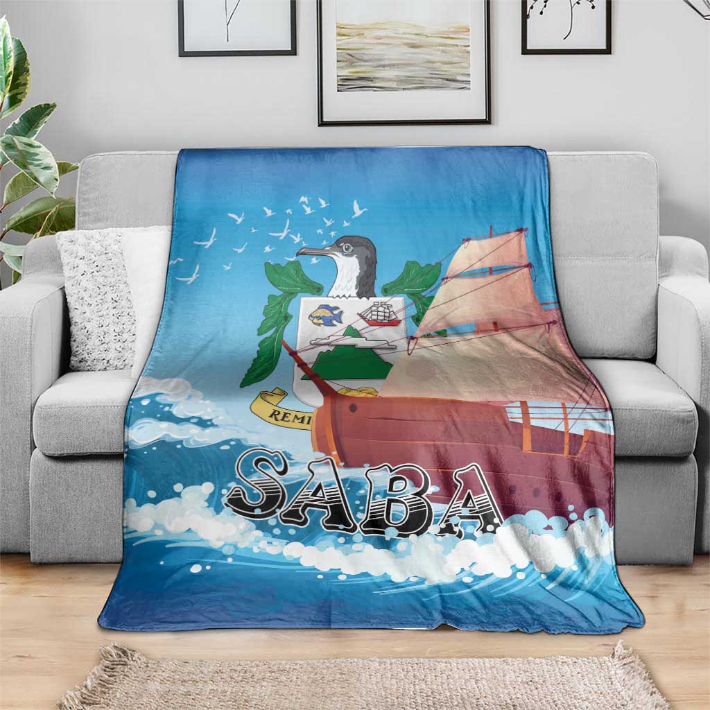 Blue sailboat-themed blanket with “SABA” text, laid across a gray sofa