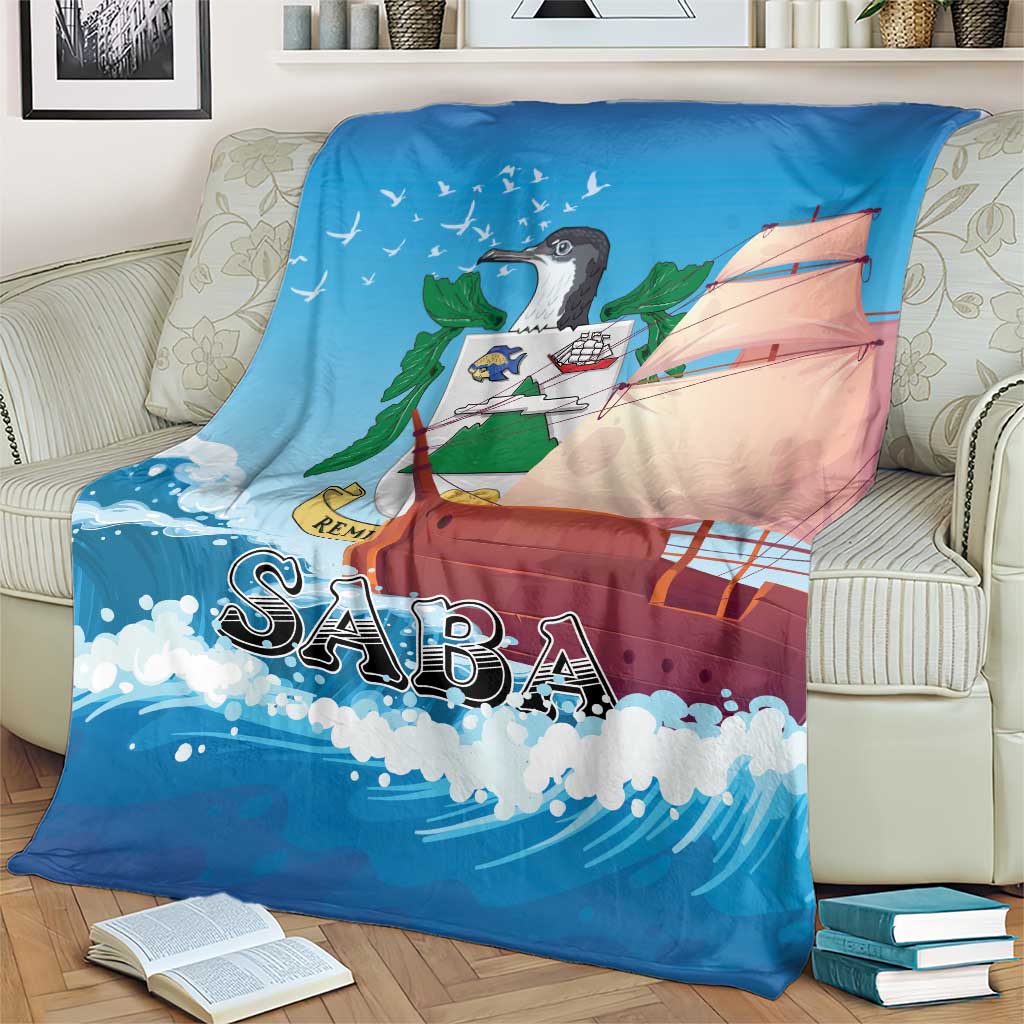 Blue throw blanket with sailboat art and “SABA” lettering, draped on a striped couch