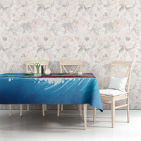 Blue sailboat tablecloth on a dining table with floral chairs and ocean wave artwork