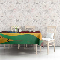 Red tablecloth with tropical motif, green and yellow curved bands, on dining table with chairs.
