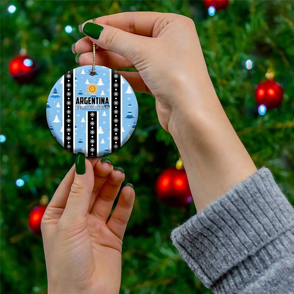 Blue circle Argentina Feliz Navidad ornament held by hand, striped with gold sun and snow trees.