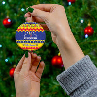 Round ceramic Venezuela Feliz Navidad ornament held by a hand with gold hanging string