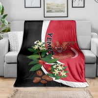 Yemen flag-style blanket on gray sofa: red center, black borders, and crest print.