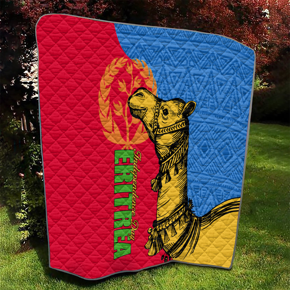 Folded quilt on grass with red, blue, and yellow sections and golden camel graphic.