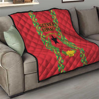 Red quilted blanket on sofa with central Guinea-Bissau emblem and green vine border