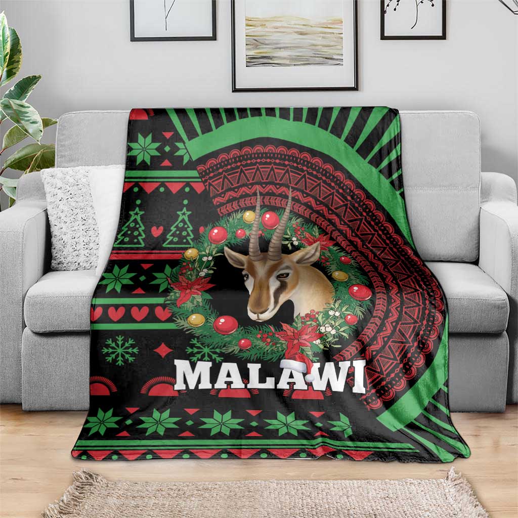 Black Christmas blanket on grey sofa, Malawi wreath design with gazelle and red-green accents