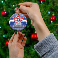 Blue ceramic round Christmas ornament with matryoshka Santa figures, held by hands, gold loop