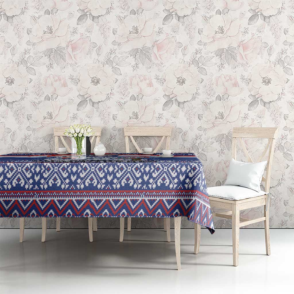 Blue patterned Christmas tablecloth on dining table with floral wall backdrop.