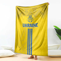 Yellow Ukraine blanket with large 'UKRAINE' logo and blue trident stripes, folk texture