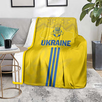 Yellow Ukraine blanket with blue striped 'UKRAINE' graphic, folded corner on floor