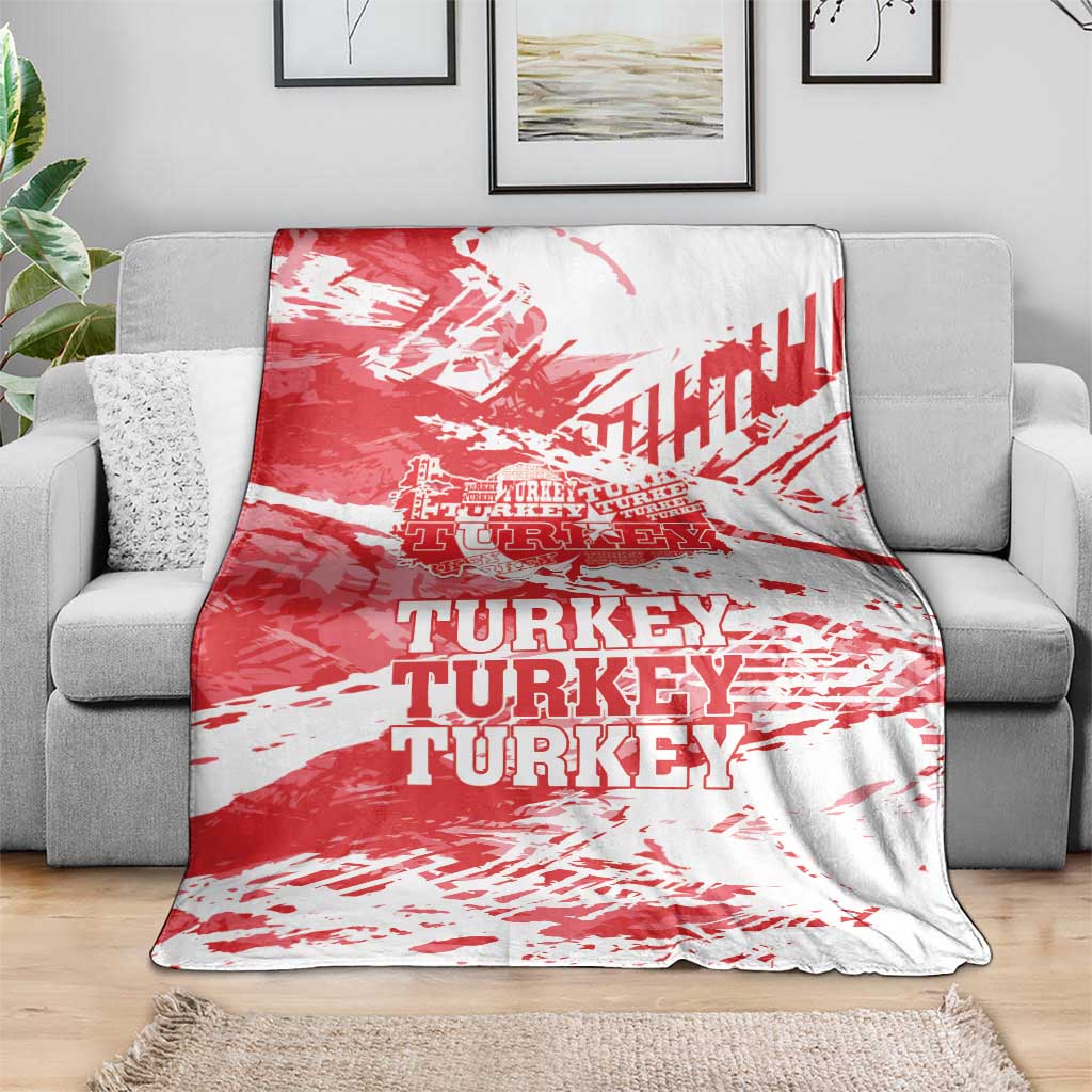 Red and white Turkey blanket with repeating TURKEY text, laid over gray sofa.
