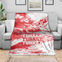 Red and white Turkey blanket with repeating TURKEY text, laid over gray sofa.