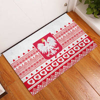 White rubber doormat laid at entry with red Polish crest and decorative folk bands