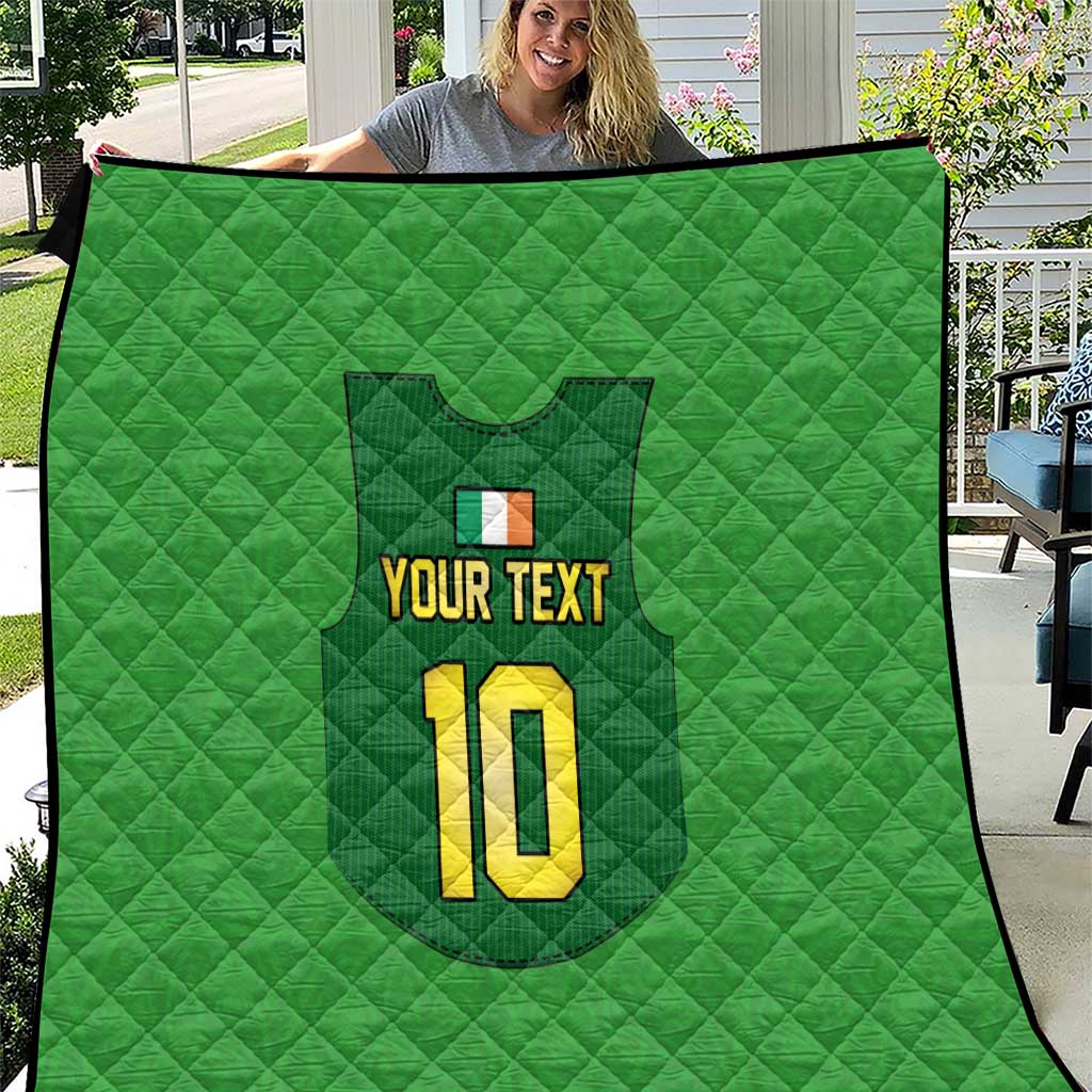 Green quilt held up outdoors, quilted pattern with crest, “YOUR TEXT”, and yellow “10”.